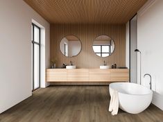 a bathroom with wood flooring and white bathtub next to two round mirrors on the wall