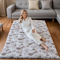 a woman sitting on top of a mat in front of a gray couch with pillows