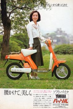 a woman standing next to an orange scooter on the grass with trees in the background