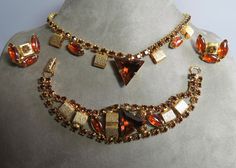 "Here's an attractive set featuring large triangle cut topaz color center stones set between marquise shaped topaz cabochons.  Textured gold  metal squares accent the stones, and all are set along rows of linking topaz smaller rhinestones.  These pieces are unsigned, but have some characteristics of Juliana or Kramer jewelry, and have obvious quality.  The necklace measures 14\" long (a true choker), bracelet is 7\" long and clip on earrings are about 1\".  This set is in beautiful condition wit Gold Jewelry With Gemstone Accents For Evening, Diamond-shaped Gold Jewelry For Party, Gold Diamond-shaped Party Jewelry, Gold Jewelry Sets With Stones For Party, Formal Jeweled Costume Jewelry Sets, Formal Costume Jewelry Sets With Jewels, Formal Gold Jewelry Sets With Gemstones, Gold Link Necklace, Fancy Stones