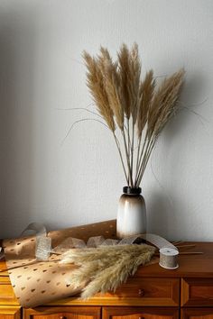 a vase filled with dry grass sitting on top of a wooden dresser