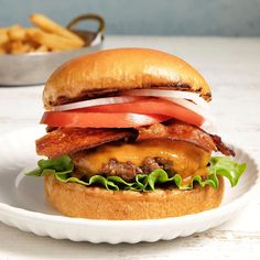 a bacon, tomato and lettuce burger on a bun with fries in the background