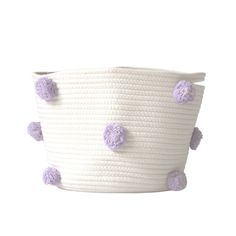 a white basket with purple pom - poms on the handles and bottom is shown