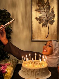 a woman in hijab holding up a cake with lit candles on it while sitting at a table