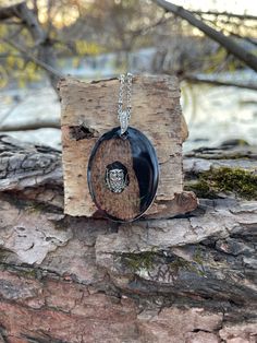 a wooden block with a black and white pendant hanging from it's side on a tree branch