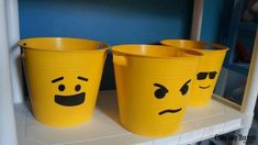 three yellow buckets with faces painted on them sitting on a shelf in a room