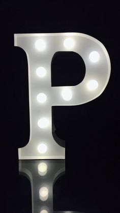 the letter p is lit up with light bulbs on it's sides and sits in front of a black background