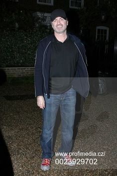 a man standing in the middle of a driveway at night with his hands in his pockets