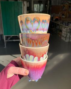 a person holding three bowls in their hand with different designs on them, all stacked high