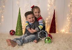 two young children sitting next to each other in front of christmas trees and garlands