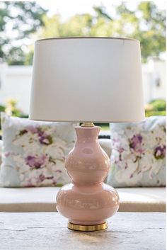 a pink lamp sitting on top of a table next to a pillow covered couch in a living room