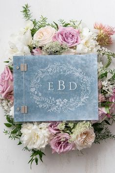 a blue book surrounded by flowers and greenery on a white background with the word e b d