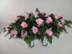 pink roses and greenery are arranged on a white surface with two black metal hooks