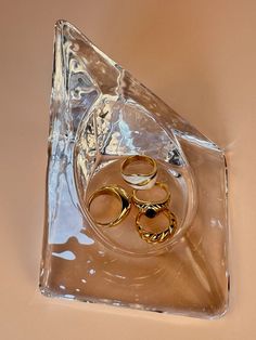 three gold wedding rings sitting on top of a clear pyramid shaped object with one ring in the middle