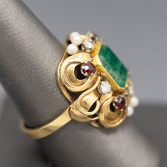 This knockout of a ring bring back visions of Renaissance jewelry- rich in colors and intricate in design. The ring features a center emerald cut emerald which is bezel set. The emerald has a closed back so we can't calculate the weight precisely, however it measures 10mm x 8.5mm, roughly calculating to 3.00ct. The stone is framed by four diamonds that measures 2.5mm each, totaling 0.24cttw. 2.8mm garnets accent the corners and the center top and bottom are highlighted by three seed pearls each. Seed Pearl, Bring Back, Bezel Setting, Emerald Cut, In Design, Statement Ring, Statement Rings, Garnet, Emerald