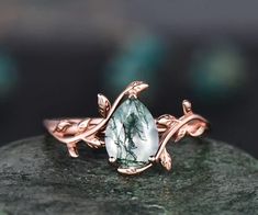 a rose gold ring with a large green stone in the center and leaves on it