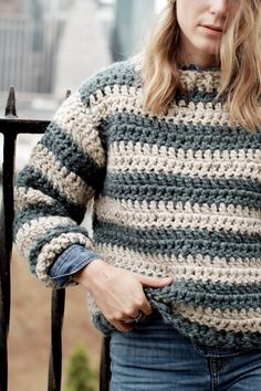 a woman standing next to a fence wearing a striped sweater