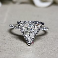 a white diamond ring sitting on top of a stone surface with diamonds around it and an arrow shaped band in the middle