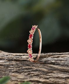 a gold ring with pink and red stones on it sitting on top of a tree branch