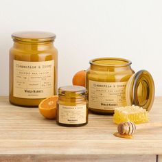 two jars of honey and an orange slice on a wooden table with a wood spoon