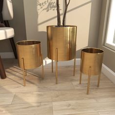 three gold planters sitting on top of a wooden floor