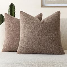 two brown pillows sitting on top of a white couch next to a green cactus plant