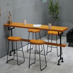 three wooden stools sitting under a table with two cups on it and a plant in the corner