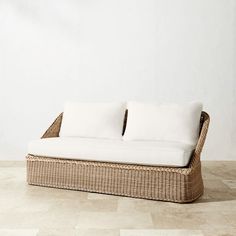 a wicker couch with two white pillows on the top and bottom, in front of a wall