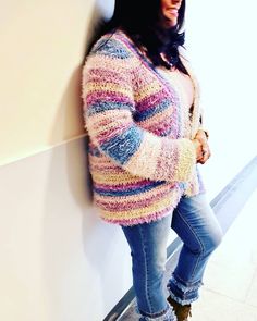 a woman leaning against a wall with her hands in her pockets and wearing jeans, sweater and boots