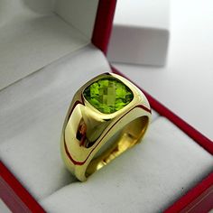 a yellow gold ring with a green stone in it's center sits inside a red box