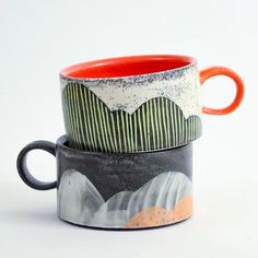 two coffee mugs sitting side by side on top of each other in different designs