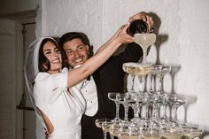 a bride and groom toasting with champagne glasses in front of a stack of wine goblets