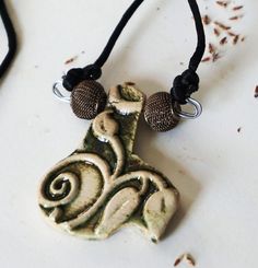 This pendant is designed with a flora and fauna motif making it a reversible necklace. The flora side displays leaves and vines. The pendant is cut to accent these. The reverse side or fauna gives the appearance of feathers or scales and forms a textured pattern. The color of the pendant is an antique gold with greenish patina. The cord is black poly satin. The two mesh antique gold beads are added as accents to the supporting nickel free wire. The pendant and beads measure approximately two(2) inches at the widest and also two(2) inches at the longest. The neck cord is a black satin poly blend and measures twenty-two(22) inches in length, letting the pendant rest at twenty-four(24) inches total. THIS IS A SLIP ON NECKLACE. NO DIFFICULT CLASPS. Ceramic Bead Jewelry, Crochet Hook Holder, Nature Motifs, Satin Noir, Art Necklaces, Flora Fauna, Ceramic Pendant, Ceramic Jewelry, Jewelry Pendant