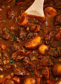 a pot filled with meat and potatoes on top of a table next to a wooden spoon