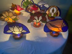 several stained glass vases sitting on top of a white table cloth covered tablecloth