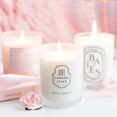 three candles sitting next to each other on top of a white table with pink flowers