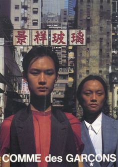 two men standing next to each other in front of tall buildings with chinese characters on them