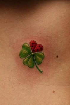 a ladybug tattoo on the back of a woman's stomach with four leaf clover