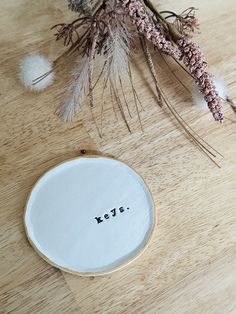 a white plate with the word keys on it next to some dried flowers and branches