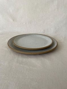 two gray and white plates sitting on top of a tablecloth covered surface with a white cloth behind them