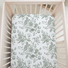 a baby crib with a white and green flowered sheet on it's side