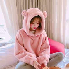 a woman in a pink bear hoodie sitting on a bed eating food from a bowl