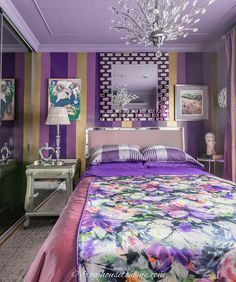 a bedroom decorated in purple and gold with a floral bed spread, chandelier, mirrored nightstands, and paintings on the wall