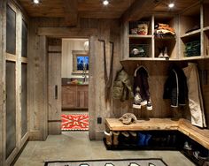 the inside of a wooden room with several coats hanging on shelves and a rug in front of it