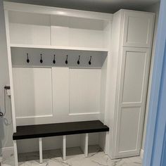 an empty bench in the corner of a room with white cabinets and coat hooks on it