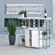 a white table with some bottles and glasses on it next to a potted plant