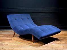 a blue chaise lounge chair sitting on top of a hard wood floor next to a black wall