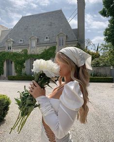 a woman holding flowers in front of a house