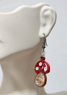 a white mannequin head with red and gold earrings on it's ear