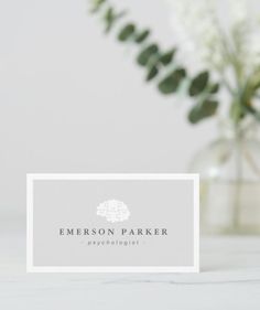 a white business card sitting on top of a table next to a vase with flowers